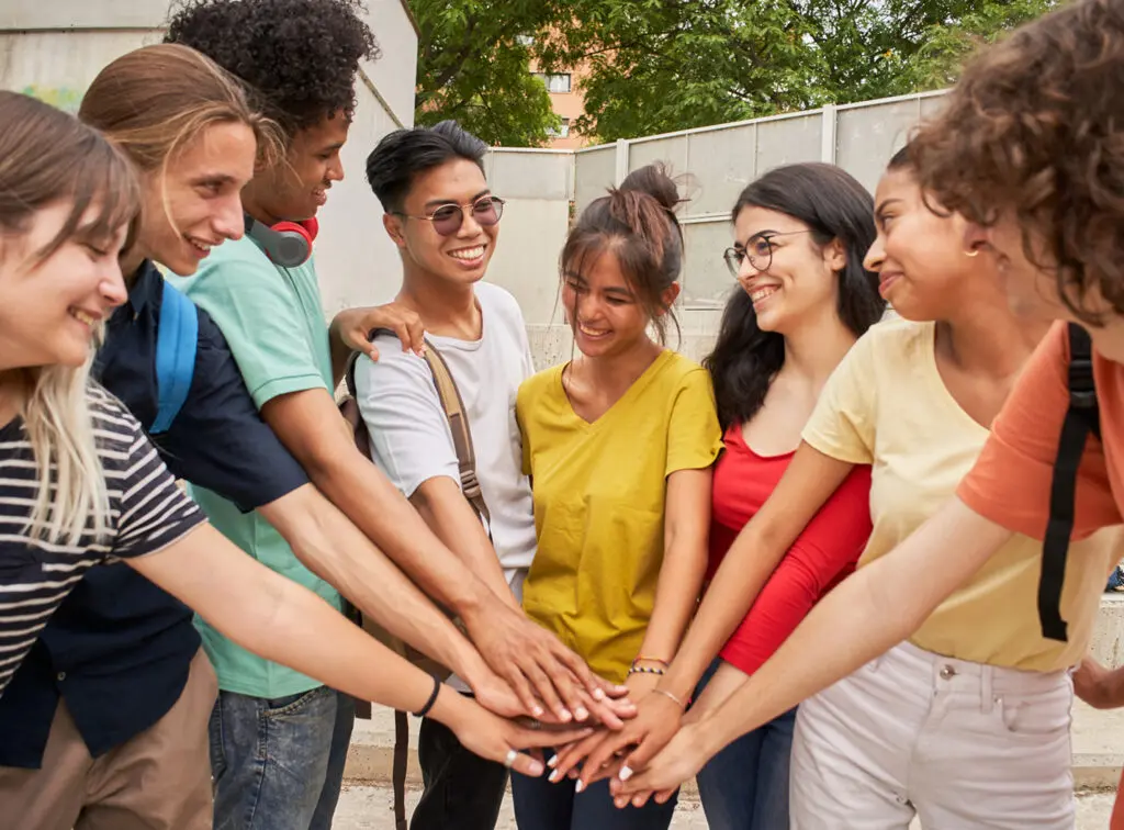 Diverse group of friends joining hands outdoors.